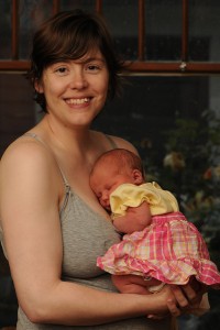 Woman wearing a gray Motherhood Maternity clip down nursing tank holding a newborn baby girl