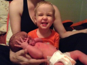 Toddler holding newborn infant wearing Honest Company disposable diaper in orange giraffe print