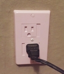 KidCo self closing outlet cover installed on wall with cord plugged in