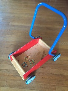 Empty walker wagon with blue handle blue wheels and red sides with stickers stuck to bottom
