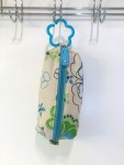 Zip up bag in green and blue floral pattern on white background hanging from infant toy link