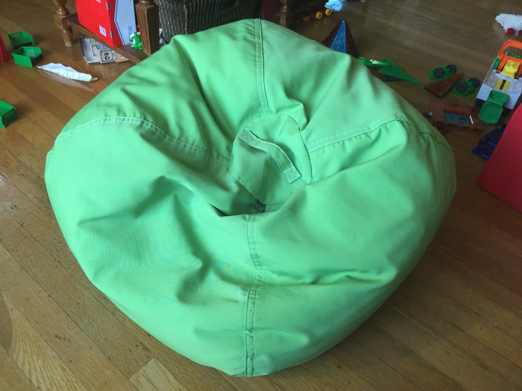 Green bean bag chair in middle of floor with toys