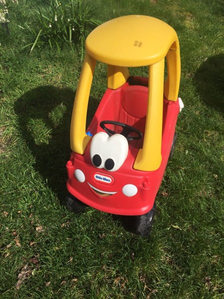 Cozy Coupe red car with yellow roof and steering wheel parked on grass