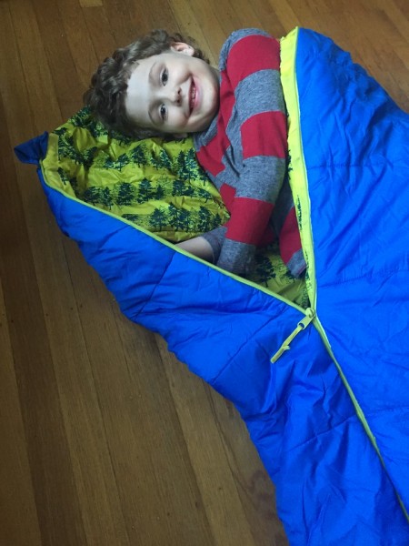 Seven year old laying in REI kids kindercone sleeping bag in blue