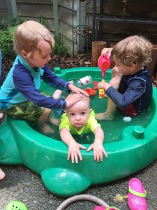 Three kids in turtle sand box from Little Tikes filled with water