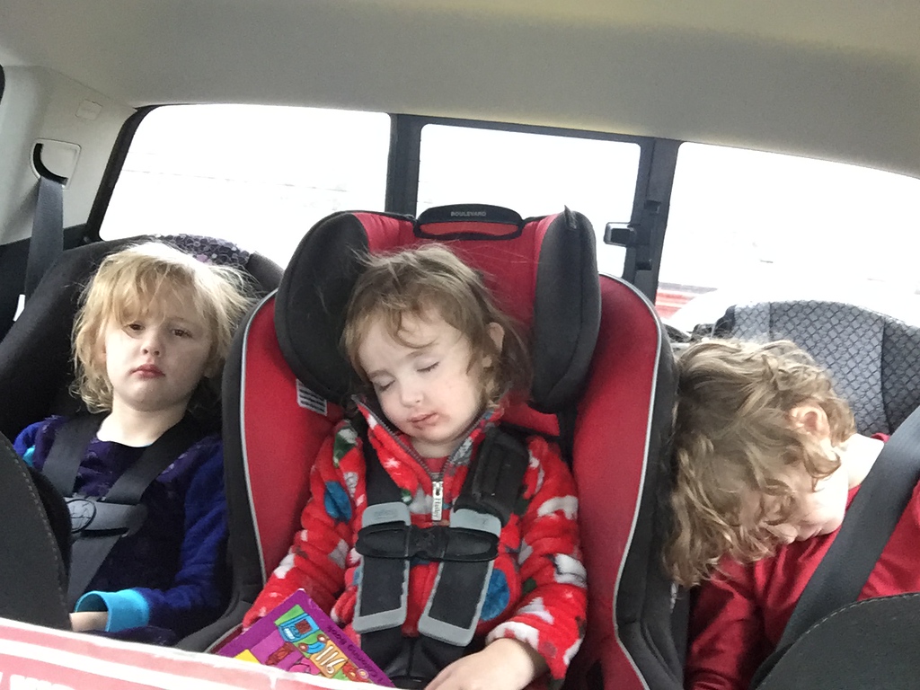 Three kids in car seats in one row two kids asleep