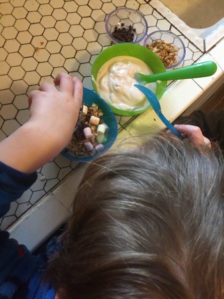 Child adding topppings to bowl of yogurt