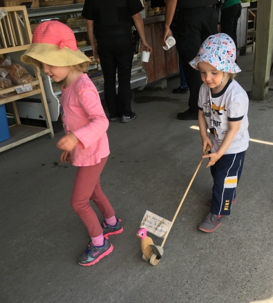 Two small kids walking wooden duck push toy on stick with pink head in outdoor market