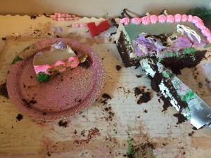 Remnants of child's chocolate birthday cake with pink and purple frosting and sparkly cake plate