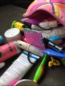 Bag with travel bathroom supplies pouring out hairspray toothbrush packing list
