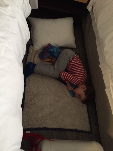 Child sleeping between two hotel beds with the JetKids BedBox at the foot of the beds