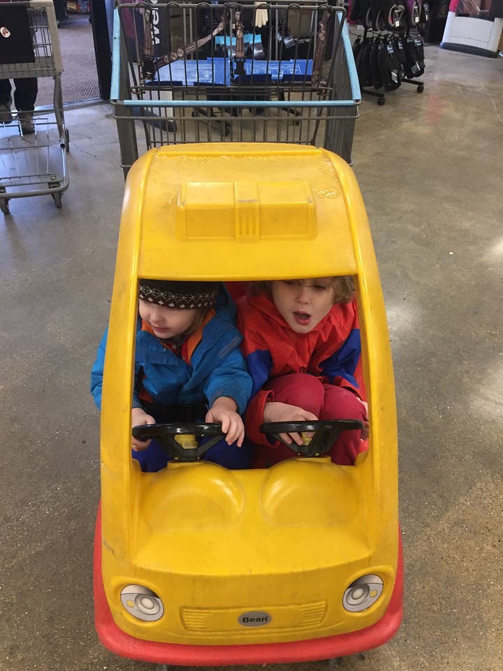 Two kids squashed into tiny car shopping cart with steering wheels