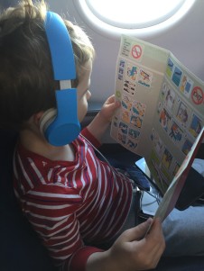 Child with headphones on board an airplane in a window seat reading emergency card