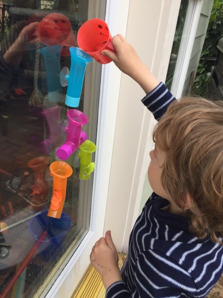 Child pouring water into Boon Building bath pipes stuck on glass door