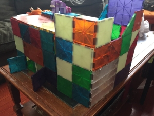 Magna-Tiles creation structure built on coffee table with Lego animals on top