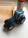 Toy tractor pictured with bottle of paint and small plastic dishes on top of paper