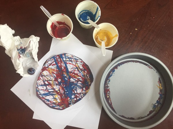 Cake pan, paper painted by rolling marbles, cups with spoons in red blue and yellow paint, paper towel with marble on it