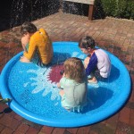 Jasonwell sprinkler play mat light blue with shark in middle and three kids sitting in it
