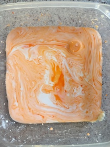 Gloop sensory play material with drops of orange food coloring swirled in container