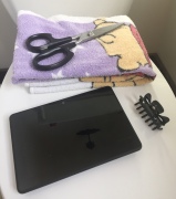 Home haircut supplies laid out on toilet seat scissors, towel, hair clip, Kindle