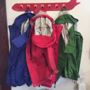 REI Rainwall Kids rain jacket in blue pink and green hanging on airplane coat hook