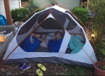 Three kids in sleeping bags inside tent set up in yard
