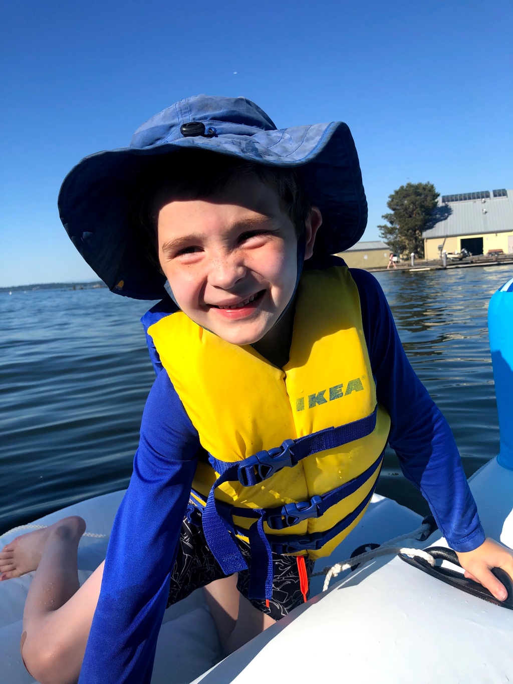 Child on boat raft float on lake wearing bright yellow Ikea life jacket and blue sun hat