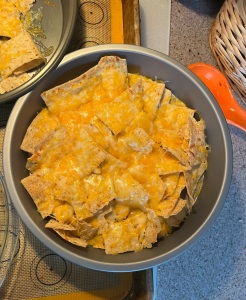 Nachos with melted cheese in cake pan cooling on stove top