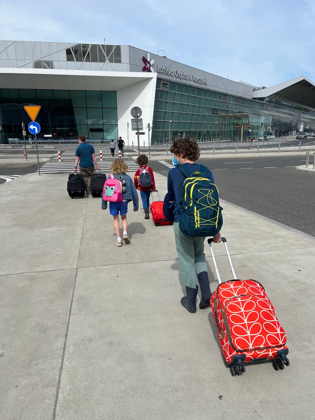 Family three kids on sidewalk pulling suitcases into airport
