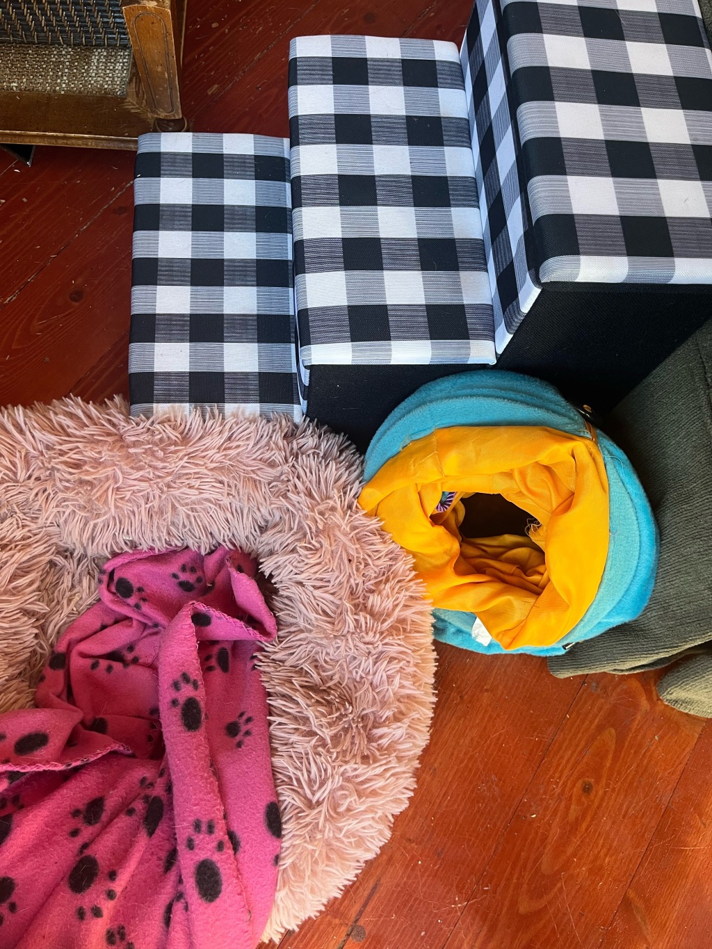 Pink fuzzy pet donut bed with hot pink paw print fleece blanket, orange and turquiose cat crinkle tunnel toy, black and white plaid dog stairs with storage