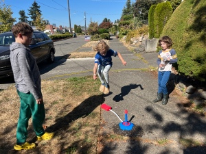 Ten year old jumping to launch Bubble Torpedo rocket toy outside on sidewalk while siblings watch