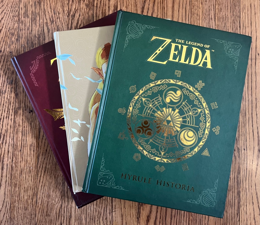 Zelda Hyrule Historia book, Official Guide, and Art and Artifacts books stacked