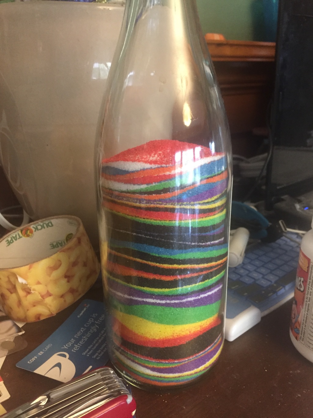 Colored sand art made by kids in clear wine bottle